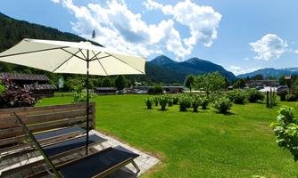 A beautiful garden with a reclining chair and a sunshade. In the background, green meadows and mountains can be seen under a blue sky with white clouds.