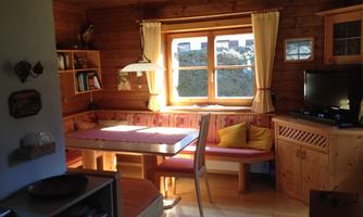A cozy room with wooden walls and windows that let in a lot of light. There is a dining table, a seating area, and a television.