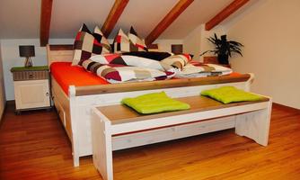 A cozy bedroom with a large bed and colorful cushions. There is also a seating bench and a small table with lamps.