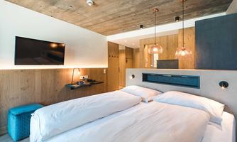 A modern bedroom with a large double bed and wood paneling. The cozy atmosphere is complemented by stylish lamps and a television.