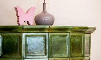 A green tile with square patterns is in the foreground. On it, there is a gray vase with a flower and a pink butterfly.