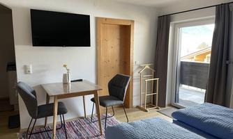 A modern room with two beds, a table, and chairs. A television on the wall and a window with a view of a balcony.