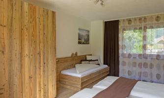 A cozy bedroom with wooden furniture and a large window. There is a bed with white sheets and soft curtains.
