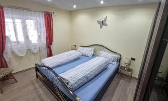A cozy bedroom with two single beds. The walls are painted light and there are red curtains as well as simple decoration.