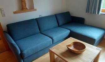 A cozy living room with a blue couch and a wooden table. A trophy and a statue hang on the wall, while daylight pours in through the window.