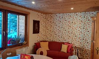 A cozy room with red sofa cushions and floral wallpaper. Through the window, one can see a wintry landscape.