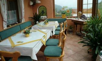 A cozy dining area with wooden furniture and green chairs. A table is nicely set, and plants create an inviting atmosphere.