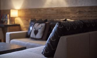 A cozy couch with decorative pillows and a wooden panel in the background. A soft light creates a warm atmosphere.
