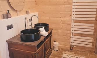 A modern bathroom with wooden ceilings and stylish sinks. The room is equipped with a carpet and a decorative mirror.