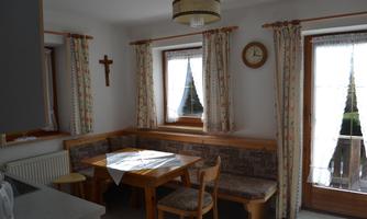 A cozy dining area with a wooden table and benches. The windows are adorned with curtains, and the room has a warm, inviting atmosphere.