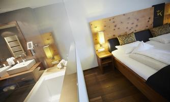A modern hotel room with a large bed and comfortable pillows. In the background, there is an elegant bathroom with a bathtub and wooden details.