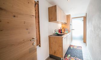 A modern kitchen with wooden cabinets and a bright atmosphere. The floor is decorated with a colorful rug.