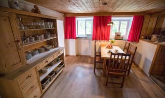 A cozy dining area with a wooden table and chairs. In the background, there is a wooden shelf with dishes and a warm, inviting atmosphere.