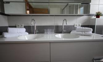 A modern bathroom with a double sink. Clean towels and glasses are ready, and the mirror reflects the space.