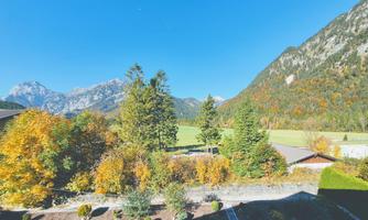 A picturesque landscape with mountains in the background and colorful autumn trees. In the foreground, well-kept gardens can be seen.