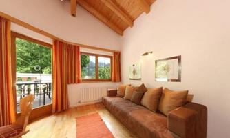 A cozy living space with a sofa and warm colors. Large windows provide a view of the greenery and let in plenty of daylight.
