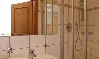 A modern bathroom with a glass shower and a sink. The walls are brightly tiled and the room is well lit.