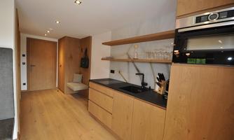 A modern kitchen with wooden-colored cabinets and a dark countertop. The space is bright and open, with a simple design.