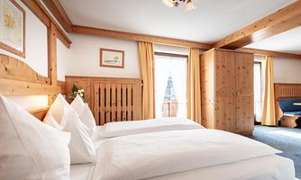 A cozy bedroom with wooden furniture and two beds. Bright curtains and a window create a friendly atmosphere.