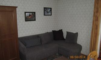 A cozy living room with a gray sofa and a wooden crate. Two pictures hang on the wall, and the room is decorated with rugs.