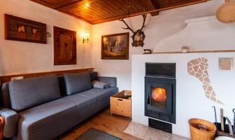A cozy living room with a gray sofa and a wood stove. The walls are adorned with traditional pictures and decorations.