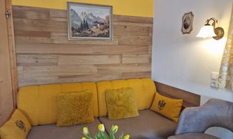 A cozy living room with a yellow couch and a wood panel wall decor. Fresh tulips in a vase are on the table.