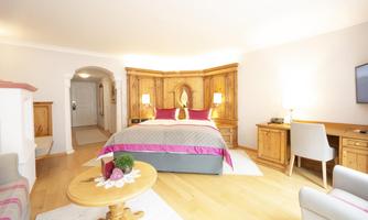 A stylish room with a large bed and wooden furniture. The room is bright and cheerful, with a desk and a television.
