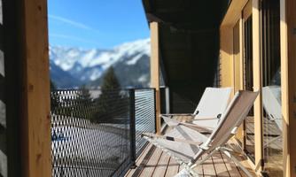 A cozy terrace with loungers and a view of snow-covered mountains. The sky is clear and blue.