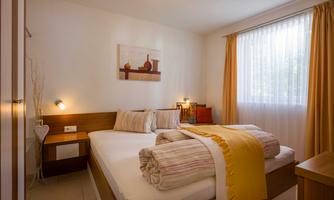 A cozy bedroom with a double bed and warm colors. The room has large windows that let in plenty of light and is tastefully decorated.