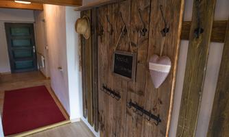 A narrow hallway with wooden paneling and a rustic wooden door. A hat and a heart hang on the door, and the floor is covered with a red carpet.