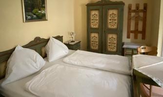 A cozy bedroom with two beds and traditional furniture. A painting hangs on the wall, and a wooden wardrobe stands in the room.