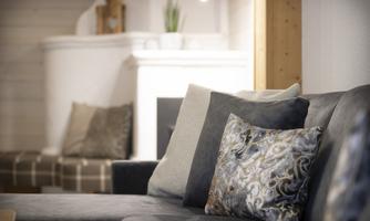 A cozy living room with a dark gray sofa and decorative cushions. In the background, a bright fireplace and a plant are visible.