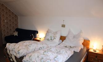 A cozy bedroom with a double bed and two nightstands. The walls are decorated with a cozy pattern, and there is a sofa in the corner.