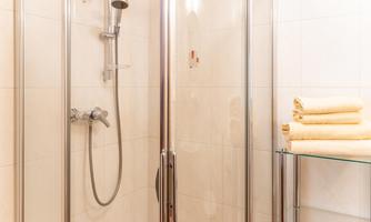 A modern shower with glass partition. Next to the shower, yellow towels are on a shelf.