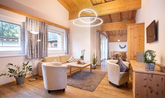 A bright and inviting living space with wood ceilings and modern furniture. The room is decorated with plants and offers a cozy atmosphere.