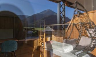 A modern room with a hanging chair and large windows. In the background, a beautiful mountain can be seen.
