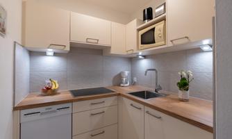 A modern kitchen with light cabinets and wooden surfaces. There is a stove, a sink, and some fruits on the countertop.