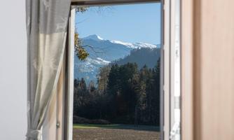 A view out the window of snow-covered mountains and trees. The sky is clear and blue, providing a serene landscape.