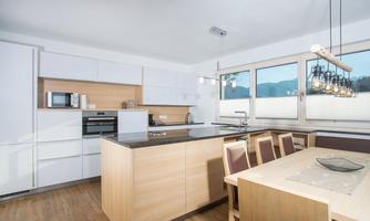 A modern kitchen with white cabinets and wooden details. The table is bright and inviting, with windows that let in plenty of daylight.