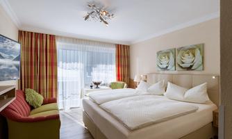 A modern bedroom with a large double bed and a cozy seating area. Large windows provide plenty of natural light and a view outside.