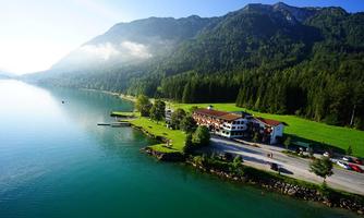 A picturesque landscape with a tranquil lake, surrounded by mountains and dense forests. At the shore stands a hotel building with a well-maintained lawn.
