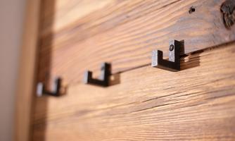 Three simple, black metal hooks on a wooden wall. The surface of the wood is warm and natural.