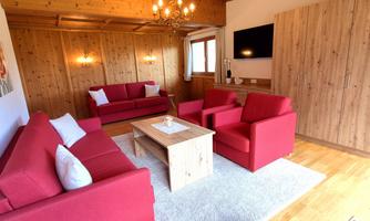 A cozy living room with red sofas and a wooden table. The room has a warm atmosphere with wooden paneling and a TV.