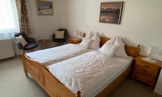 A quiet bedroom with two single beds and wooden furniture. A window lets in plenty of light, and there is a cozy armchair.