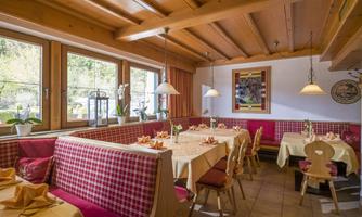 A cozy restaurant with wooden furniture and red checkered chairs. The tables are lovingly set, and the light is warm and inviting.