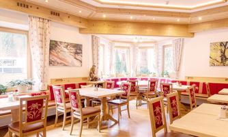 A cozy restaurant room with wooden decor and red upholstery. Large windows let in plenty of light and offer a view of the outdoors.