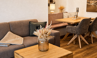 A cozy living area with a gray sofa and a wooden table.  
Decorative elements such as a bouquet of flowers and cushions give the room an inviting atmosphere.