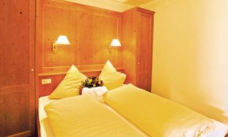 A cozy bedroom with two single beds covered with yellow bedspreads. Warm wood and soft lighting are visible on the walls.