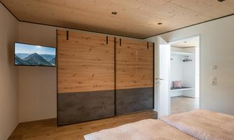 A modern bedroom with wooden paneling and a large wardrobe. A television and an open door to another room are visible.