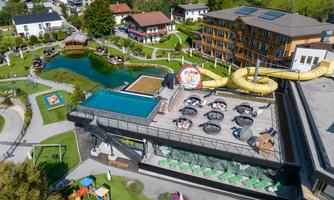 A modern resort with a pool, sun loungers, and a slide. The well-kept garden landscape and the surrounding houses create an inviting atmosphere.